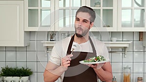 An attractive Man in an apron tastes a cooked vegan salad and enjoys it.
