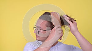 Attractive man in glasses with bristles brushes hair with large wooden brush, air blows over his face and dries hair on