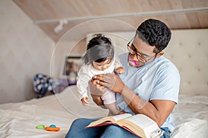 Attractive man is holding a baby girl and reading a book