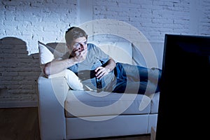 Attractive man at home lying on couch at living room watching tv looking surprised in shock