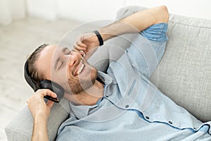 Attractive man listening music lying on the couch and listening to music on headphones