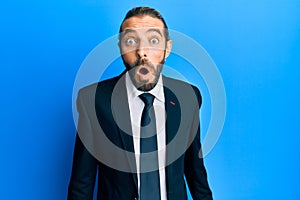 Attractive man with long hair and beard wearing business suit and tie scared and amazed with open mouth for surprise, disbelief