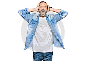 Attractive man with long hair and beard wearing casual denim jacket crazy and scared with hands on head, afraid and surprised of