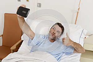 Attractive man lying on bed hospital clinic holding mobile phone taking self portrait selfie photo