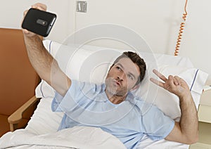 Attractive man lying on bed hospital clinic holding mobile phone taking self portrait selfie photo