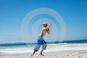 Attractive man playing frisby on beach in summer