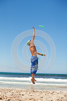 Attractive man playing frisby on beach in summer