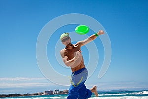 Attractive man playing frisby on beach in summer