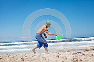 Attractive man playing frisby on beach in summer photo