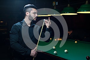 Attractive man preparing cue for playing billiard