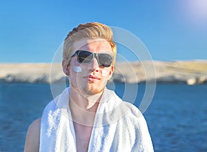 Attractive man with protective sun cream on the face for care of his body.