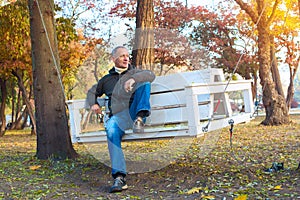 Attractive man relaxing in a autumn park, sitting on swing and