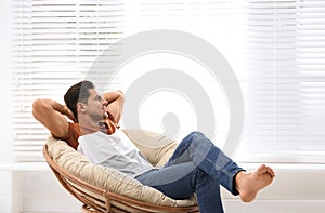 Attractive man relaxing in papasan chair near window