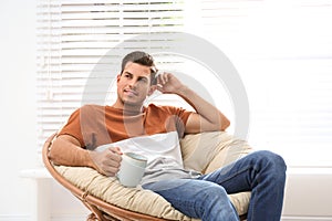 Attractive man relaxing in papasan chair near window