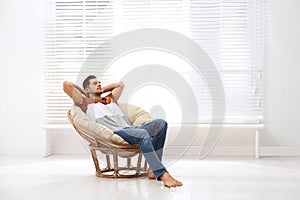 Attractive man relaxing in papasan chair near window. Space for text photo