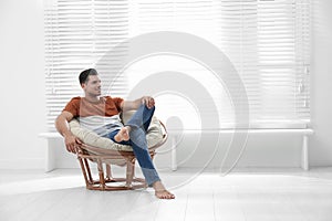 Attractive man relaxing in papasan chair near window at home photo