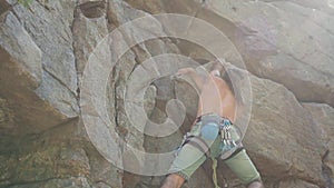 Attractive man rock climber climbs on a granite cliff, reaching and gripping hold.