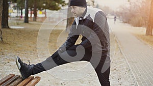 Attractive man runner doing stretching exercise preparing for morning workout and jogging in winter park