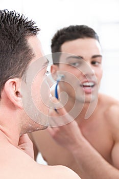 Attractive man shaving in front of bathroom mirror