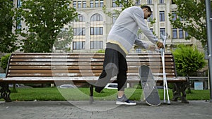 Attractive man sits on the bench in the park putting his crutches and skateboard nearby. Active life of disabled person