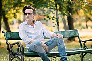 Attractive man sitting alone on the bench with cellphone
