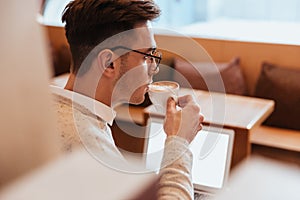 Attractive man sitting in cafe using laptop and drinking coffee.