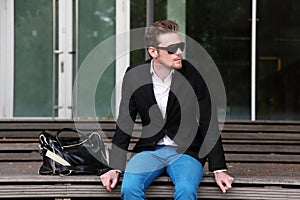 An attractive man sitting down outside wearing jeans and a blazer