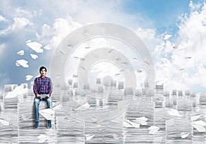 Attractive man sitting on pile of paper documents.