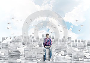 Attractive man sitting on pile of paper documents.