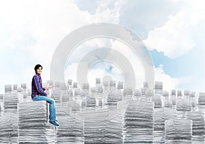 Attractive man sitting on pile of paper documents.