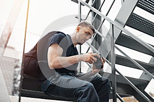 Attractive man sitting at staircase and checking photos in camera.