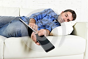 Attractive man sleeping at home couch with mobile phone and digital tablet pad in his hands