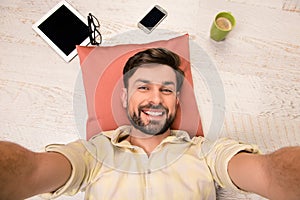 Attractive man with stubble making selfie lying on floor