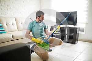 Attractive man using broom as a guitar