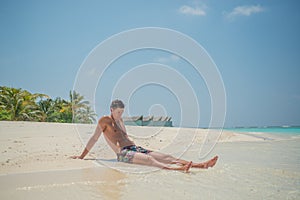Attractive man wearing swimming shorts at tropical beach at island luxury resort
