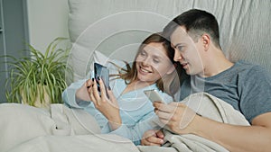 Attractive man and woman using smartphones in bed talking smiling at home