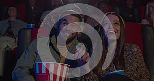 Attractive man and woman watching funny movie and smiling at movie theatre. Young couple enjoing film and talking while