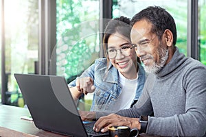 Attractive mature asian man with white stylish short beard looking at laptop computer with teenage eye glasses hipster woman in