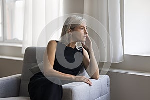Attractive mature blonde woman relaxing alone seated on cozy armchair