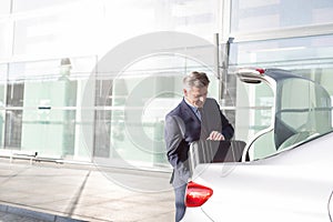 Attractive mature businessman putting his luggage on car trunk