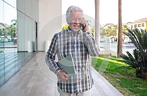 Attractive mature businessman talking on mobile phone holding laptop computer in the hand. Bearded senior man wearing eyeglasses