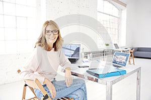 Attractive mature businesswoman looking at camera and smiling while working at office desk