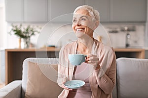 Attractive mature lady drinking fresh coffee at modern living room