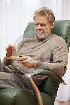 Attractive mature man relaxing in a chair and playing solitaire in a bright living room