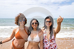 Attractive mature woman next to two young, pretty, brunette South American women in bikinis and sunglasses taking funny pictures