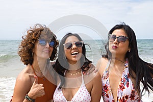 Attractive mature woman next to two young, pretty, brunette South American women in bikinis and sunglasses taking funny pictures