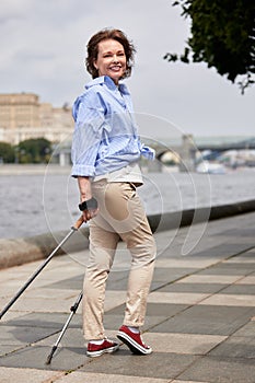 Attractive mature woman with nordic walking poles. Senior lady walking down the river embankment. Middle aged brunette