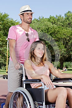 attractive man pushing parter in wheelchair through park photo