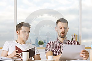 Attractive men reading book and doing paperwork