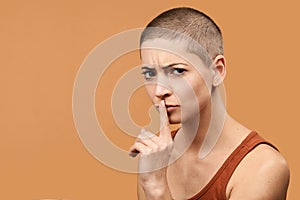 Attractive mid 30s woman pressing finger to lips as if asking to keep silent. Photo of young angry woman making Shhh gesture.